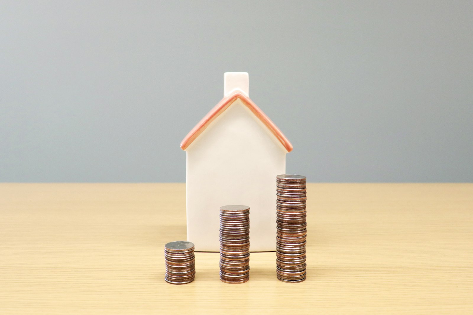 Miniatur rumah dan tumpukan koin menggambarkan berbagai jenis passive income seperti properti sewa dan dividen